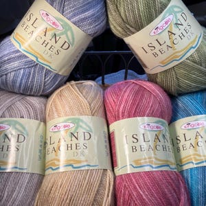 May include: Six balls of yarn in various colours, including blue, green, beige, and pink. Each ball has a label that reads "Island Beaches DK" with a palm tree graphic.