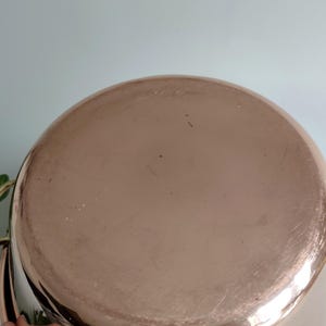 May include: A copper-coloured pot with a rounded base. The pot has a shiny, reflective surface with minor scratches. The pot's design suggests it is for cooking or serving food.