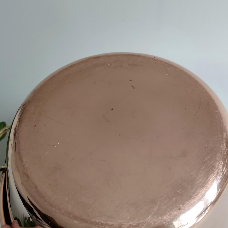 May include: A copper-coloured pot with a rounded base. The pot has a shiny, reflective surface with minor scratches. The pot's design suggests it is for cooking or serving food.