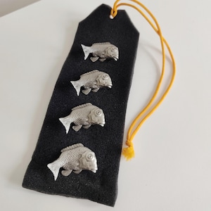 May include: A black bookmark with four silver-colored fish charms. The bookmark has a yellow cord attached at the top. The fish charms are detailed with scales and fins.