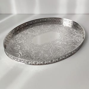 Puede incluir: Bandeja ovalada de plata para servir con intrincados diseños florales y de volutas. La bandeja tiene un borde calado decorativo y una superficie pulida y reflectante. Una pieza clásica para servir alimentos o exhibir objetos.