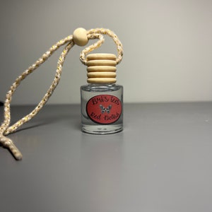 Op de afbeelding: Een doorzichtige glazen fles met een rood en wit etiket waarop "Bri's Tees Red + Delish" staat. De fles heeft een houten dop en een beige touwtje.