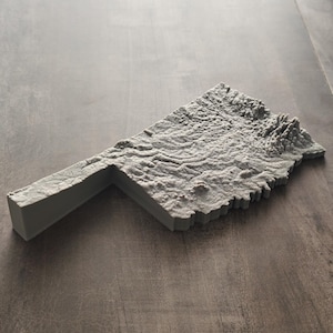 May include: A three-dimensional gray topographical map of the state of Oklahoma, featuring a textured surface that represents the varied terrain, elevations, and landscape features of the region in a solid, monochromatic, and detailed relief form.