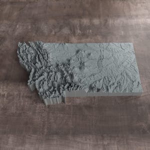 May include: A three-dimensional topographic map of the state of Montana rendered in a solid light gray color. The model features detailed relief showing mountain ranges, valleys, and plains with vertical sides that define the state's geographic borders.