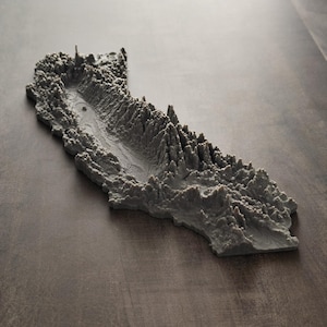 May include: A gray, three-dimensional topographical model of the state of California. The sculpture features detailed, raised relief textures representing mountain ranges, valleys, and coastal terrain, rendered in a solid, matte gray finish.