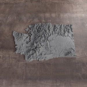 May include: A three-dimensional gray relief map of the state of Washington, showcasing detailed topographical features including mountain ranges, valleys, and coastal inlets with a textured surface finish that highlights the varied elevation.