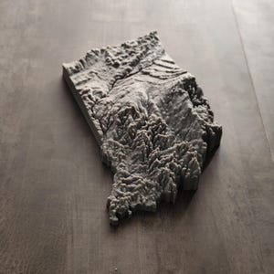 May include: A three-dimensional gray topographic map model featuring intricate relief details of a mountainous landscape. The physical sculpture displays varied elevations, deep valleys, and jagged ridges, rendered in a solid, monochromatic gray finish.