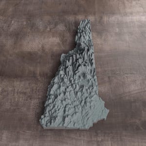 May include: A three-dimensional topographical map of the state of New Hampshire, rendered in a solid matte gray finish. The model features detailed relief elevations representing the mountainous terrain and geographical features of the state.