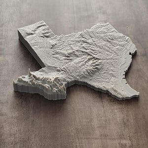 May include: A three-dimensional, light gray topographical map of the state of Texas. The object features a textured surface that accurately represents the varied elevation, mountain ranges, and terrain details across the entire state geography.
