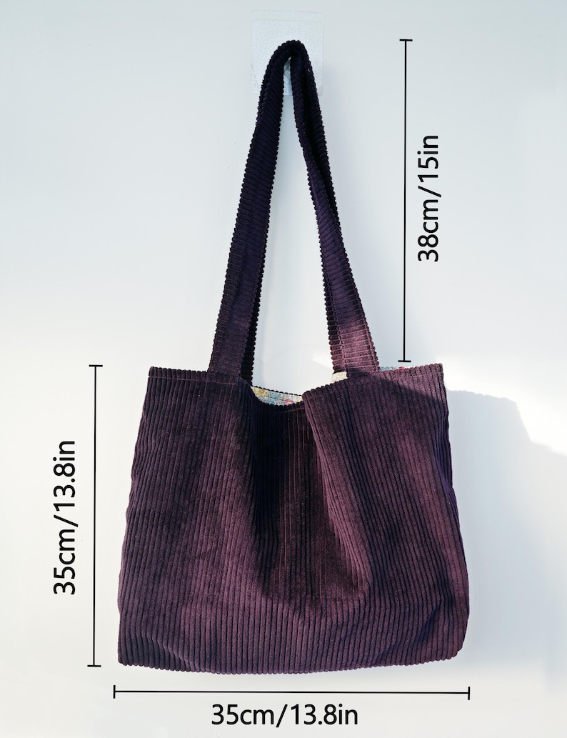 Op de afbeelding: Een pruimkleurige corduroy tote bag met een rechthoekige vorm. De tas is 35 cm breed, 35 cm diep en 38 cm hoog. De tas heeft twee lange hengsels en hangt tegen een witte muur.