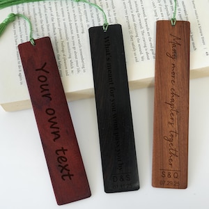 Può includere: Tre segnalibri in legno con nappe verdi. Uno è rosso scuro con il testo "Your own text", un altro è nero con "What's meant for you wont pass you by", e l'ultimo è marrone con "Many more chapters together".