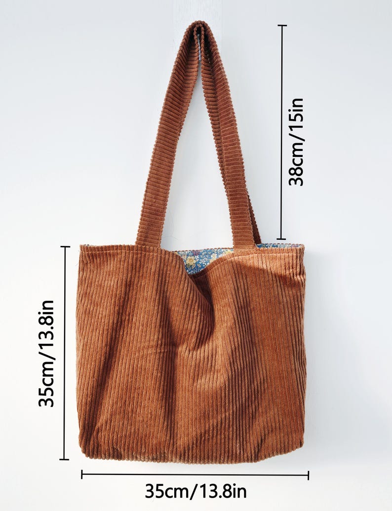 May include: A brown corduroy tote bag with a floral patterned lining. The bag measures 13.8 inches wide, 13.8 inches high, and has 15-inch-long handles. The bag is made of a soft, ribbed fabric and is designed for carrying items.
