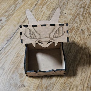 May include: A wooden box with a dragon face on the lid. The box is open and the inside is empty.