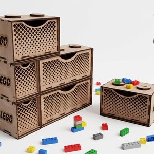 May include: Wooden Lego storage boxes in a light brown color. The boxes are stacked and feature a lattice design on the front. The word "LEGO" is printed on the side of the boxes. Colorful Lego bricks are scattered around the boxes.