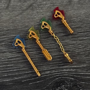 May include: Four ornate, gold-colored keys with colorful accents. Each key features a different colored top: blue, green, yellow, and red. One key is connected to a gold chain. The keys are arranged on a dark wood-grain surface.