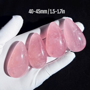 Puede incluir: Cuatro piedras de cuarzo rosa, cada una con forma de lágrima, se muestran sobre una superficie blanca. Las piedras miden aproximadamente 40 a 45 mm.