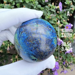 May include: A polished spherical azurite and malachite stone featuring deep blue and green mineral patterns. Text on the image indicates a diameter of 43mm and a weight of 98.5g. The sphere is labelled with the letter A, with imperial equivalents.