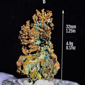 Puede incluir: Esp&eacute;cimen mineral de cobre natural con una superficie rugosa y texturizada. El mineral presenta tonos dorados, verdes y amarillos. El esp&eacute;cimen mide 32 mm de altura y pesa 4,9 g.