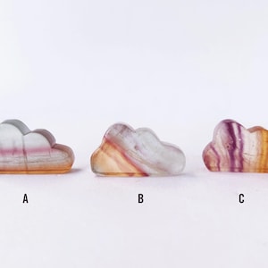 Peut inclure: Trois sculptures en cristal de fluorine en forme de nuage dans des tons de violet, rose et blanc. Les sculptures sont disposées en rangée de gauche à droite, étiquetées A, B et C.