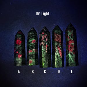 May include: Five green and red crystal points labelled A to E under UV light. The crystals glow brightly in shades of green and red.