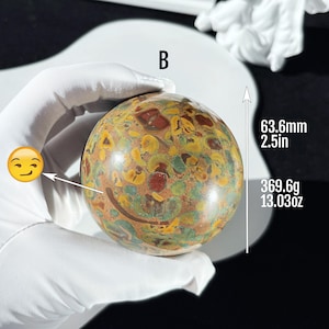 May include: A decorative stone sphere with a mottled pattern in brown, green, and red. The sphere is 6.36cm in diameter and weighs 369.6g. The letter "B" is visible on the top of the stone.