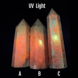 Puede incluir: Tres obeliscos de cristal facetados bajo luz ultravioleta. Los cristales tienen un brillo c&aacute;lido, naranja y rosa con toques de verde y azul. El texto "UV Light" est&aacute; en la parte superior y las letras A, B y C en la parte inferior.