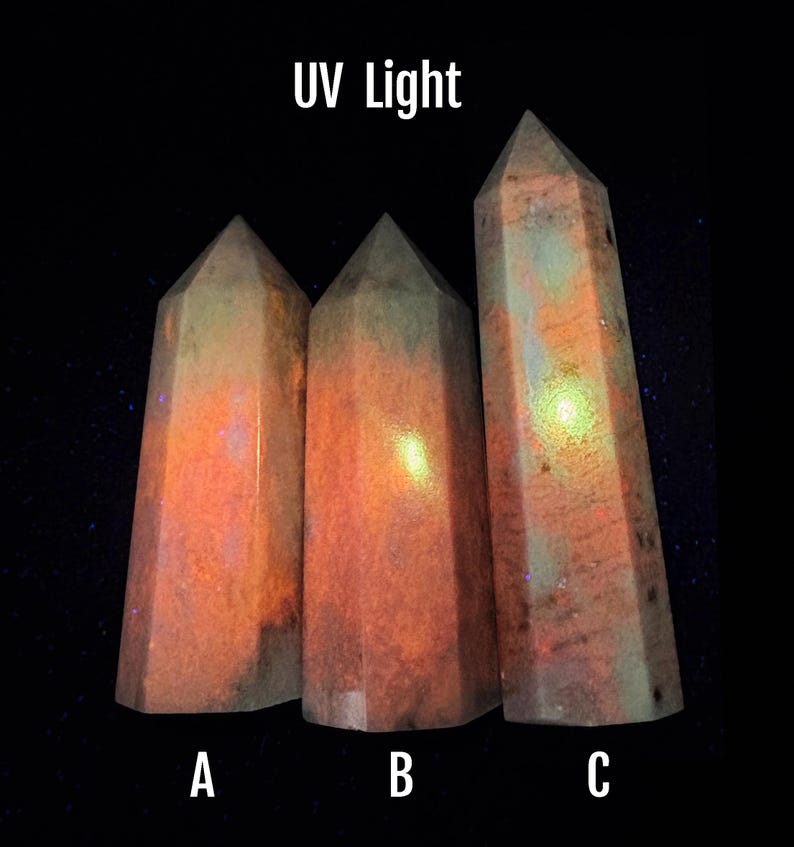 Puede incluir: Tres obeliscos de cristal facetados bajo luz ultravioleta. Los cristales tienen un brillo c&aacute;lido, naranja y rosa con toques de verde y azul. El texto "UV Light" est&aacute; en la parte superior y las letras A, B y C en la parte inferior.