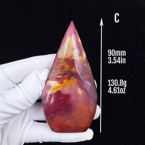 Puede incluir: Una escultura de piedra pulida en forma de lágrima con un patrón jaspeado de tonos rojo intenso, burdeos y amarillo con vetas oscuras. El objeto está marcado con una C, mide 90 mm de altura y pesa 130,8 g.