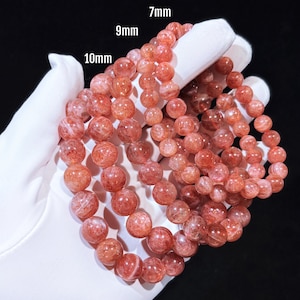 May include: Three strands of sunstone bead bracelets in varying sizes: 7mm, 9mm, and 10mm. The beads are a warm reddish-orange colour with a translucent, speckled appearance. The bracelets are displayed against a white background.