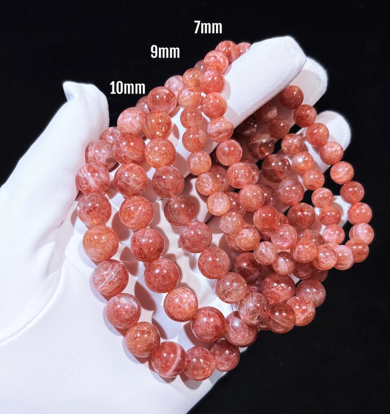 May include: Three strands of sunstone bead bracelets in varying sizes: 7mm, 9mm, and 10mm. The beads are a warm reddish-orange colour with a translucent, speckled appearance. The bracelets are displayed against a white background.