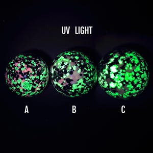 Peut inclure: Trois objets sphériques étiquetés A, B et C, exposés sous une lumière UV. Chaque sphère présente un motif tacheté de noir, de blanc et de points vert néon lumineux. Le texte UV LIGHT est placé au-dessus des sphères sur un fond sombre.