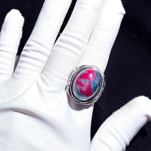 May include: A silver ring featuring a large oval-shaped gemstone. The gemstone is a blend of pink and green hues.
