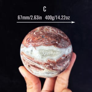 Peut inclure: Une sphère d'agate de grande taille, de 67 mm (2,63 po), avec un motif tourbillonnant de rouge, de blanc et de brun. La sphère est lisse et polie, et elle pèse 400 g (14,22 oz).