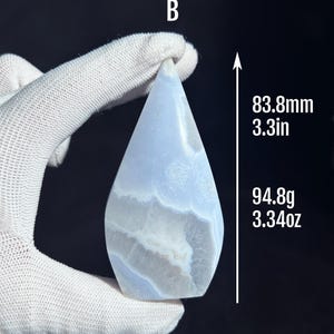 May include: A teardrop-shaped blue agate crystal with white and gray banding. The crystal is 3.3 inches tall and weighs 3.34 ounces.