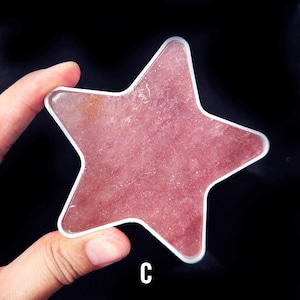May include: A pink star-shaped piece of polished rose quartz. The quartz is set in a clear plastic frame.
