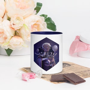 May include: White ceramic mug with a navy blue rim. The mug features a colorful illustration of a person with white hair and a blue and purple robe holding a glowing orb. The background is a dark purple with a geometric pattern.
