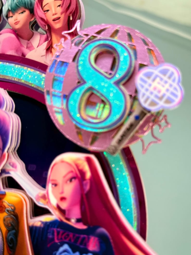 May include: A colorful cake topper featuring a large teal number 8 with glitter accents, set against a pink disco ball design. The topper includes cartoon figures and a microphone, suggesting a birthday or celebration theme.