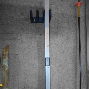 Könnte beinhalten: Ein silbernes Metall-Wasserwaage mit einem schwarzen Kunststoffsockel und einer schwarzen Kunststoffhalterung oben. Das Wasserwaagen-Werkzeug ist an einer Wand montiert.