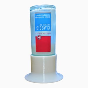Op de afbeelding: Een heldere glazen fles met een blauw en rood etiket, met de tekst "CLASSIC" en "ANTI-TRANSPIRANT 50ml", staat in een witte, uitlopende basis. De fles bevat een witte vloeistof. Het etiket bevat Duitse tekst.