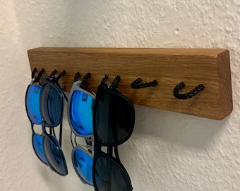 May include: A wooden wall-mounted sunglasses holder with black rope loops. Four pairs of sunglasses with blue lenses are hanging on the loops.