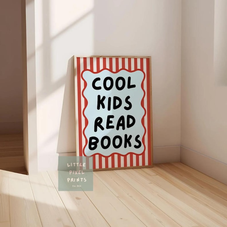 May include: A framed print with the text "COOL KIDS READ BOOKS" in black on a light blue background. The frame has a red and white striped border. The print is leaning against a wall on a wooden floor.
