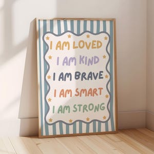 May include: A framed wall art print featuring a light blue and white vertical striped background. The centre has a white scalloped-edge rectangle with yellow stars and the text: I AM LOVED, I AM KIND, I AM BRAVE, I AM SMART, I AM STRONG.