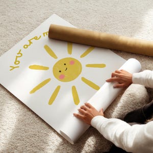 May include: A white poster with a yellow sun illustration and the words "You are my" in yellow. A rolled-up poster and a brown cardboard tube are also visible.