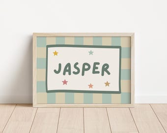 May include: A rectangular framed print featuring the name JASPER in dark green letters centred on a cream background. The design includes a dark green border and five small multi-coloured stars. The background has vertical stripes in light blue and beige.
