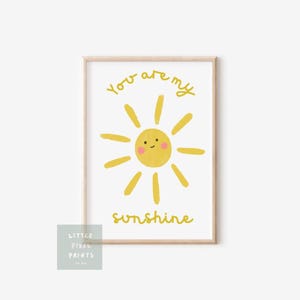 May include: A framed print featuring a yellow cartoon sun with a smiling face and radiating beams. The words "You are my sunshine" are written in yellow script. A small logo is in the lower left corner.