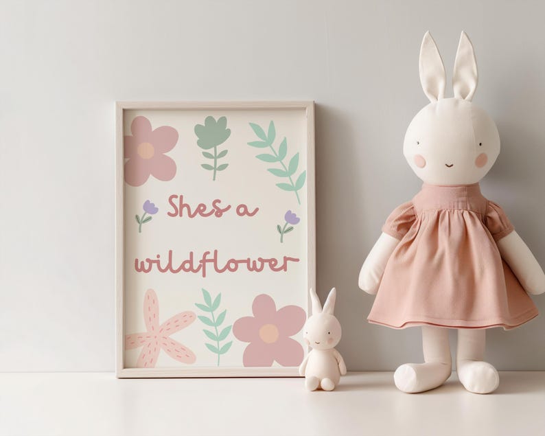 May include: A framed print with the text "Shes a wildflower" and floral illustrations in pink, green, and purple. A large stuffed bunny wearing a pink dress and a small bunny figurine are next to the print.