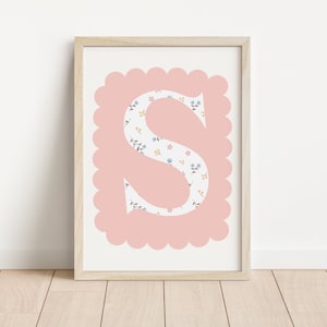 May include: A pink and white floral print letter S in a scalloped frame. The letter is printed on white paper and framed in a light wood frame.