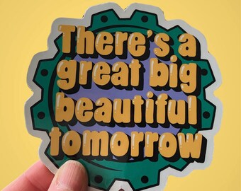 Könnte beinhalten: Ein Aufkleber mit dem Text "There's a great big beautiful tomorrow" in einem Retro-Schriftstil. Der Aufkleber hat einen zahnradartigen Rand in Grün und Schwarz, mit einem lila und weißen Hintergrund. Der Aufkleber wird vor einem gelben Hintergrund gehalten.