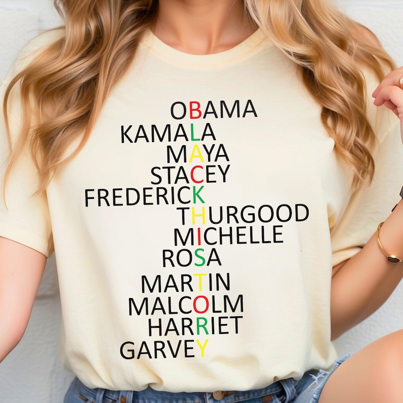 Może przedstawiać: Ż&oacute;łta koszulka z czarnym, zielonym i czerwonym wzorem, kt&oacute;ry tworzy napis "BLACK" z nazwiskami wybitnych Afroamerykan&oacute;w: Obama, Kamala, Maya, Stacey, Frederick, Thurgood, Michelle, Rosa, Martin, Malcolm, Harriet i Garvey.
