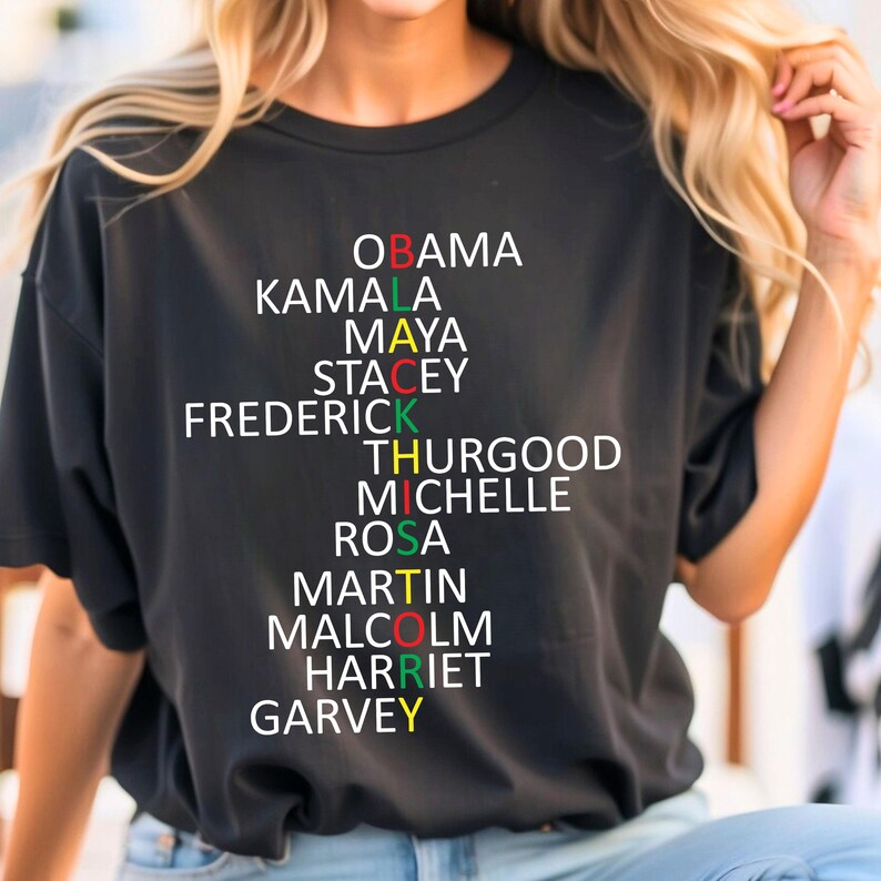 Może przedstawiać: Czarny T-shirt z wzorem układanki słownej przedstawiający nazwiska wybitnych Afroamerykan&oacute;w. Nazwiska to Obama, Kamala, Maya, Stacey, Frederick, Thurgood, Michelle, Rosa, Martin, Malcolm, Harriet i Garvey.